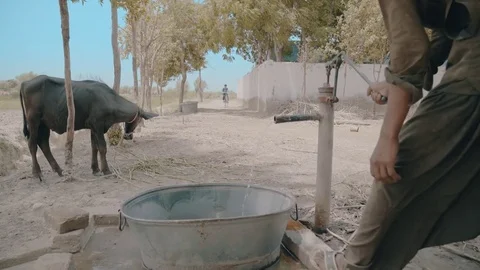 School boy cycles towards his home as villager uses Hand pump in a small Village Stock Footage