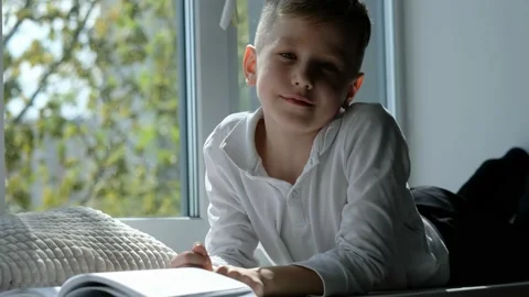 School boy reading on windowsill, enjoying sunny weather, looking at camera Stock Footage 194766492