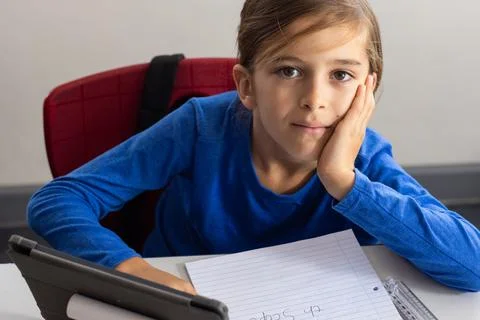 In school, boy using tablet and writing in notepad, looking at camera Stock Photos