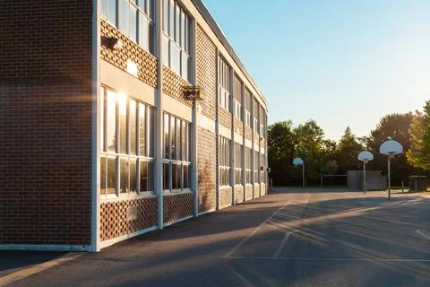 School building exterior and school yard with basketball court in the evening Stock Photos