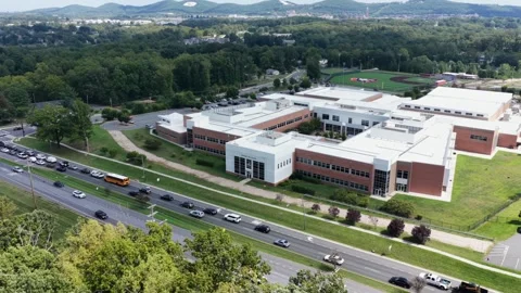 School bus travels multilane road beside modern high school campus, brick and Stock Footage 345700438