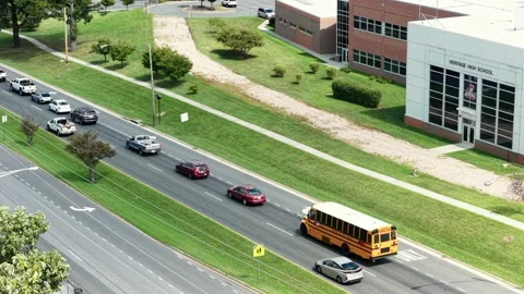 School bus turns onto multilane road beside modern school building, queued Stock Footage 345727831