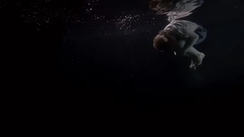 School child in fetal position is floating under water surface in dark river or Stock Footage 153610337