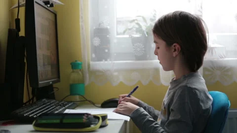 School child, sitting at the table with laptop, writing school tasks while ho Stock Footage 146890548