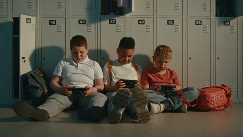 School Children Relax by Lockers While Sharing Content on Portable Devices Stock Footage 342048853