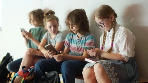 School children sit on a bench at school with their smartphones. Internet Stock Footage 109497209