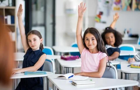 School children sitting at the desk in classroom on the lesson, raising hands. Stock Photos