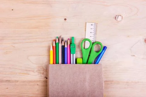 School concept. Colored pencils, scissors, ruler, compasses in brown paper ba Stock Photos