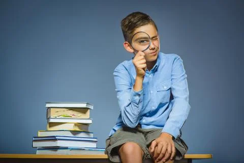 School concept. doubt boy sitting on desk and looking into a magnifying glass Stock Photos