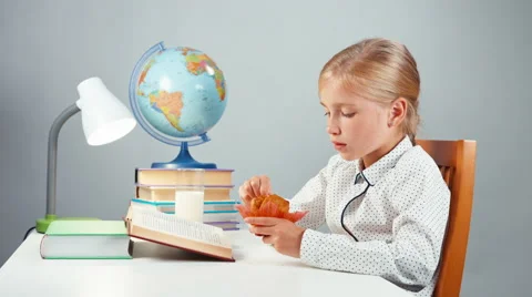School girl 7-8 years reading book eating muffin sitting at the table Stock Footage