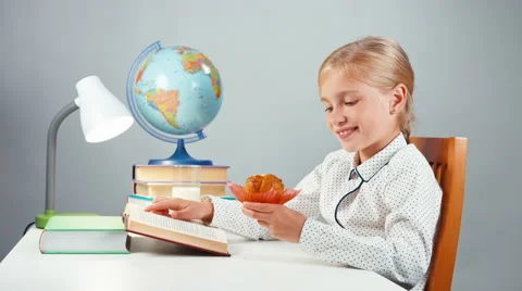School girl 7-8 years reading book and eating muffin Stock Footage