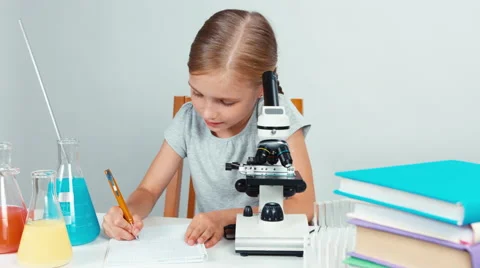 School girl using microscope and something writing in her exercise book Stock Footage 65457396