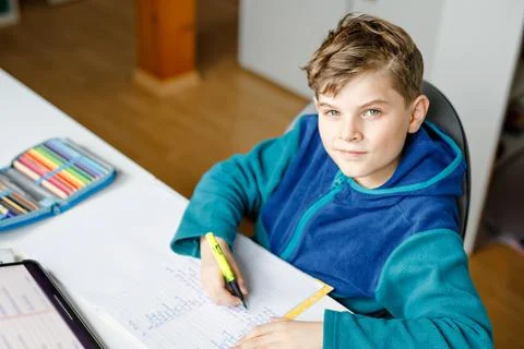 School kid boy learning at home with tablet for school. Adorable child making Stock Photos