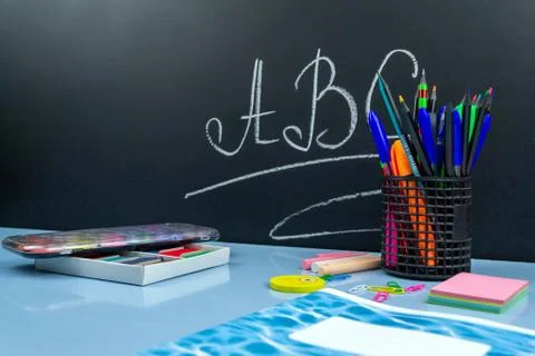 School supplies on a blue table, in the back a black chalkboard with letters Stock Photos