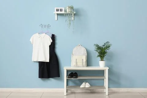 School uniform, backpack, and shoes on a bench with a clock and plant against Stock Photos