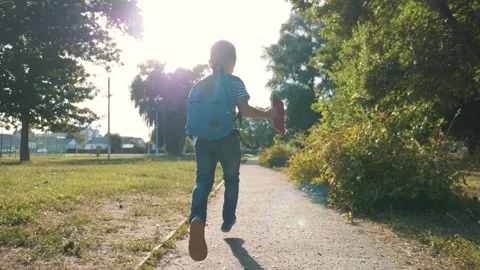 A schoolboy with a backpack and a book in the Park. A happy child runs to school Stock Footage 137884209