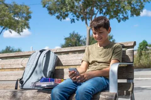 Schoolboy on bench taking break using mobile Stock Photos