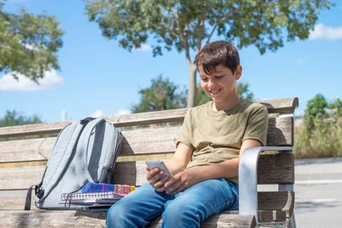 Schoolboy on bench taking break using mobile Stock Photos
