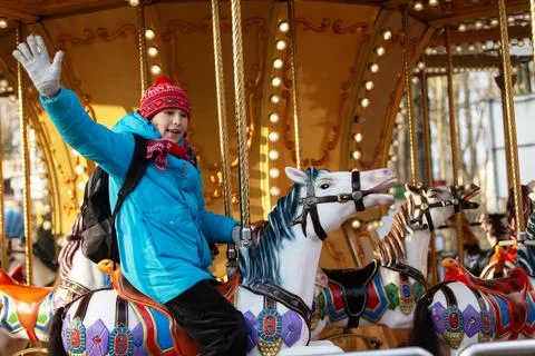 A schoolboy boy with a backpack waves his hand on a carousel in a brightly .. Stock-Fotos