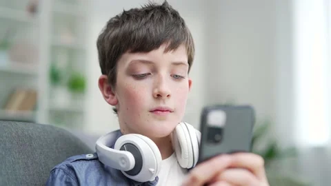 Schoolboy boy uses smartphone while sitting on the couch at home. Indoor. Close Stock Footage 238633339