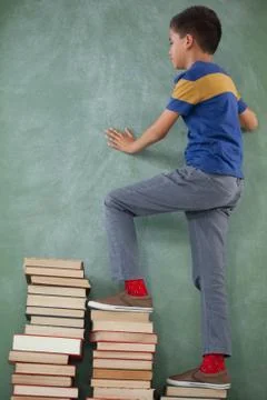 Schoolboy climbing steps of books stack Foto stock