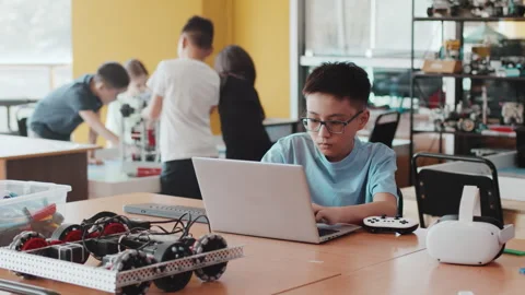 Schoolboy coding on a laptop sitting at the desktop with a joystick, VR headset Stock Footage 249357035