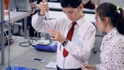 A schoolboy demonstrates how to add chemicals into a tube. Stock Footage