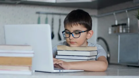 A schoolboy does homework while sitting in the kitchen at the table using a lot Stock Footage 127938524