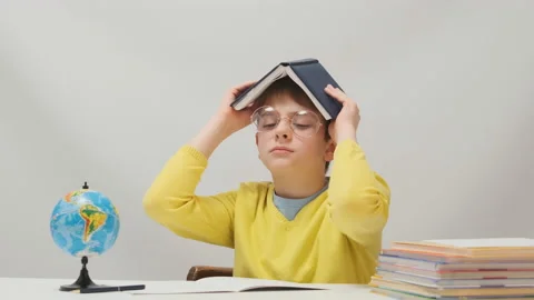 Schoolboy doing homework fooling around and holding book over head as roof Video stock 172490455