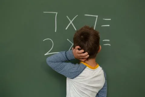 Schoolboy doing math on greenboard in a classroom Stock Photos