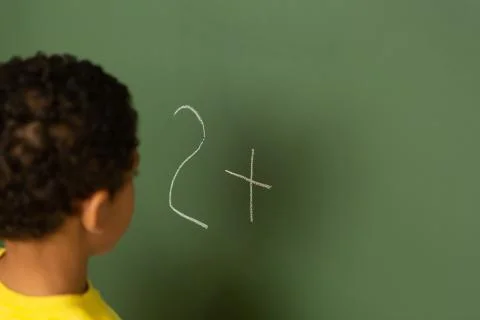 Schoolboy doing math on greenboard in a classroom Stock Photos