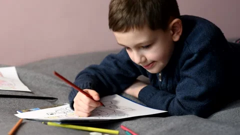 Schoolboy draws with colored pencils on sofa at home. Chooses pencils by color Stock Footage 170262898