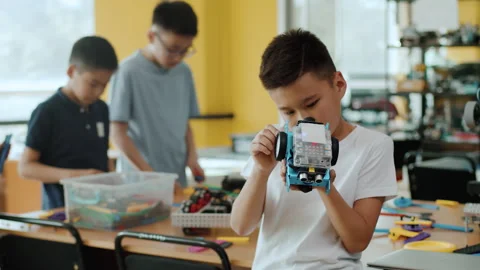 Schoolboy exploring the assembled robot and smiling in a class with the other Stock Footage 242169975