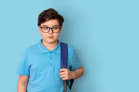 A schoolboy in glasses, with backpack, on blue background, looking away Stock Photos