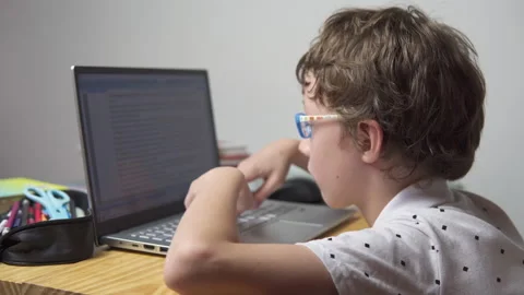 Schoolboy in glasses is using tablet computer for studying at home 스톡 동영상 348549476