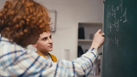 Schoolboy helping classmate with a math problem, solving equation on board Stock Footage 250334295