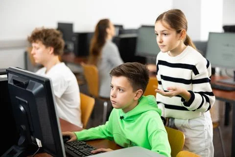 Schoolboy helping classmate to solve computer trouble in classroom Stock Photos