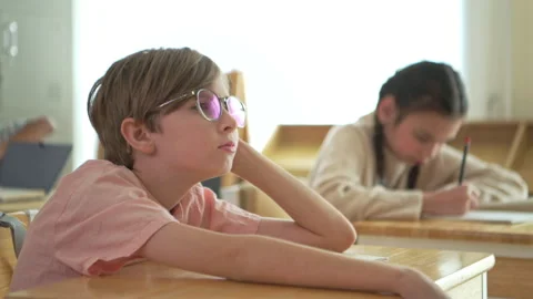 Schoolboy looking bored and distracted in classroom while classmates study Stock Footage 339326208