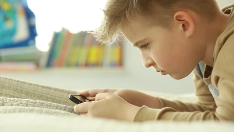  Schoolboy looking at a smart phone while lying on the bed.  Stock Footage 106396845