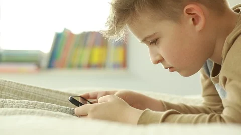  Schoolboy looking at a smart phone while lying on the bed.  Stock Footage 106396861