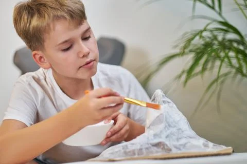 Schoolboy makes creative project in form of papier mache mountain. Stock Photos