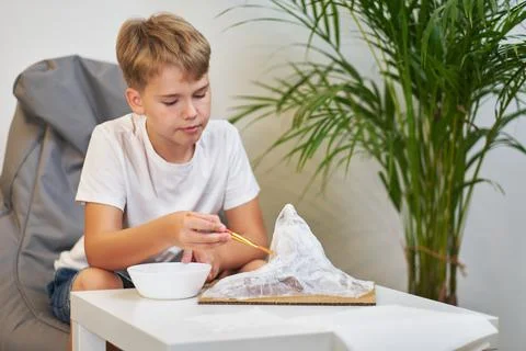 Schoolboy makes creative project in form of papier mache mountain. Stock Photos