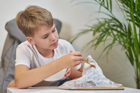 Schoolboy makes creative project in form of papier mache mountain. 스톡 사진