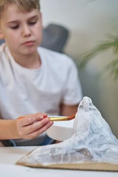 Schoolboy makes creative project in form of papier mache mountain. Stock Photos