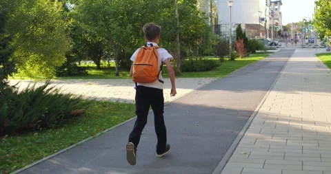 Schoolboy runs along urban path toward school with backpack. Young student Stock Footage 346042230