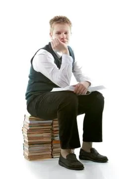 The schoolboy in a school uniform sits on a pack of books, with the opened bo Stock Photos