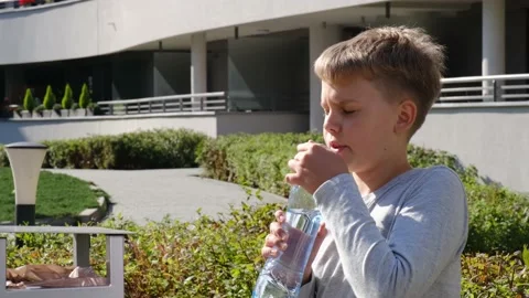 Schoolboy sitting on bench and drinks clear still water from plastic bottle. Stock Footage 160924892