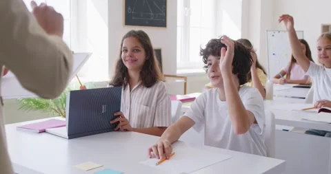 Schoolboy sitting in the classroom raising hand up and giving right answer to Stock Footage 331195642