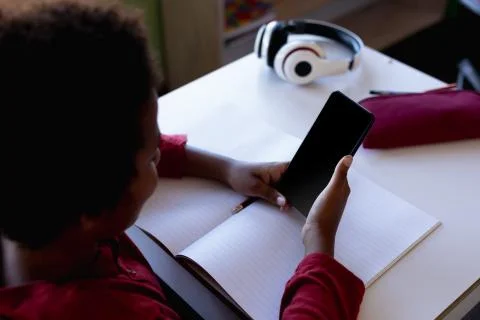 Schoolboy sitting at a desk using a smartphone in an elementary school classroom Foto stock