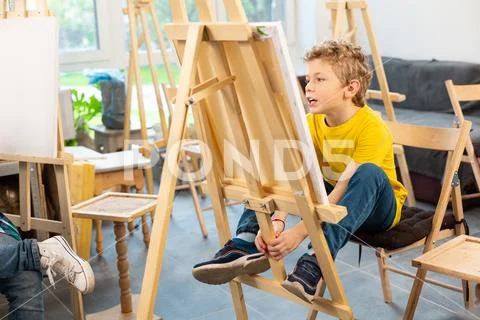 Schoolboy sitting near painting easel in art school Stock Photos